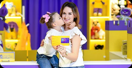 Мама целует дочку, которая держит свидетельство о рождении игрушки